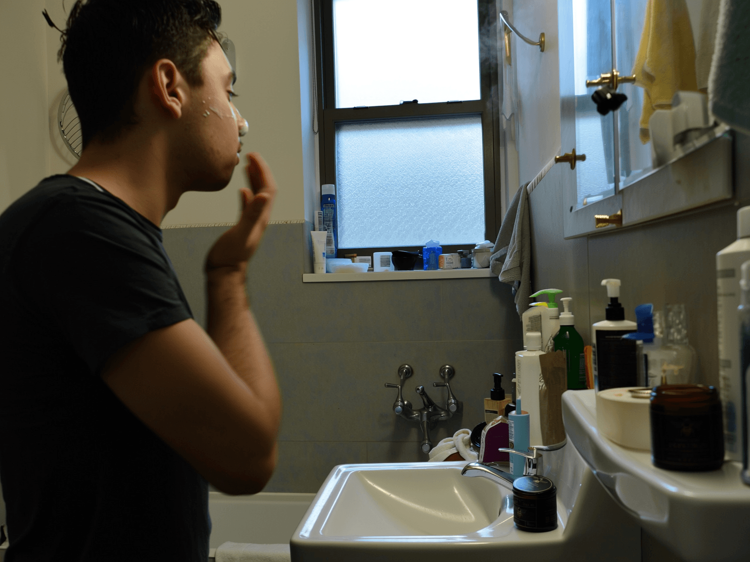 Young man applying balm to his jaw in front of a bathroom mirror after shaving